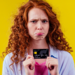 Confused redhaired ginger curly woman holding plastic creditcard