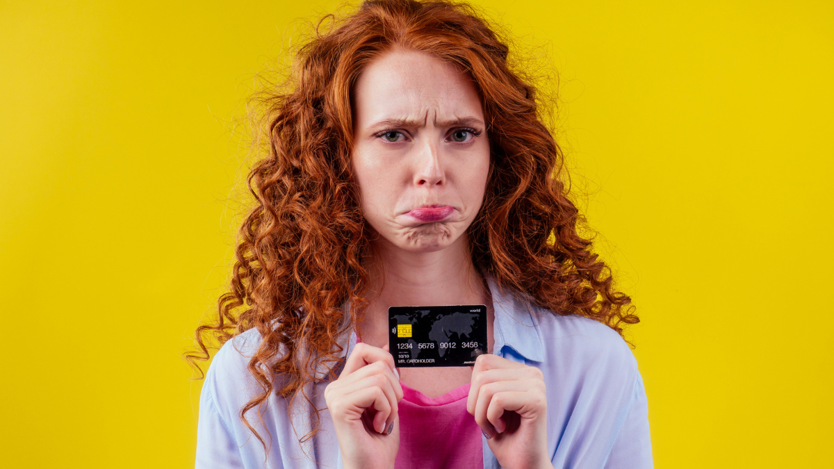 Confused redhaired ginger curly woman holding plastic creditcard