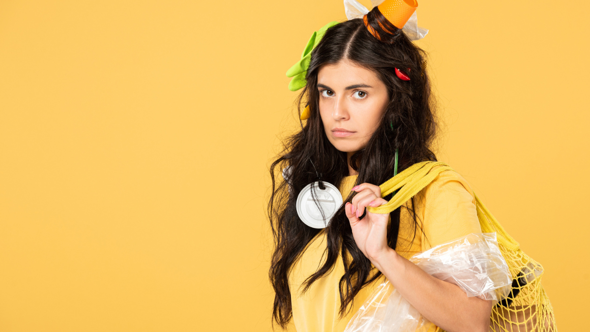 Upset girl with trash in hair holding bag with rubbish isolated on yellow.