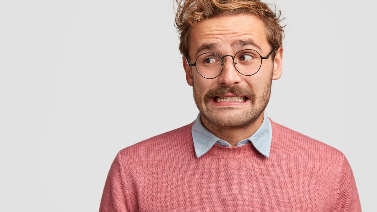 Puzzled attractive bearded emotive male wonk in spectacles, looks with worried embarrassed expression aside,.
