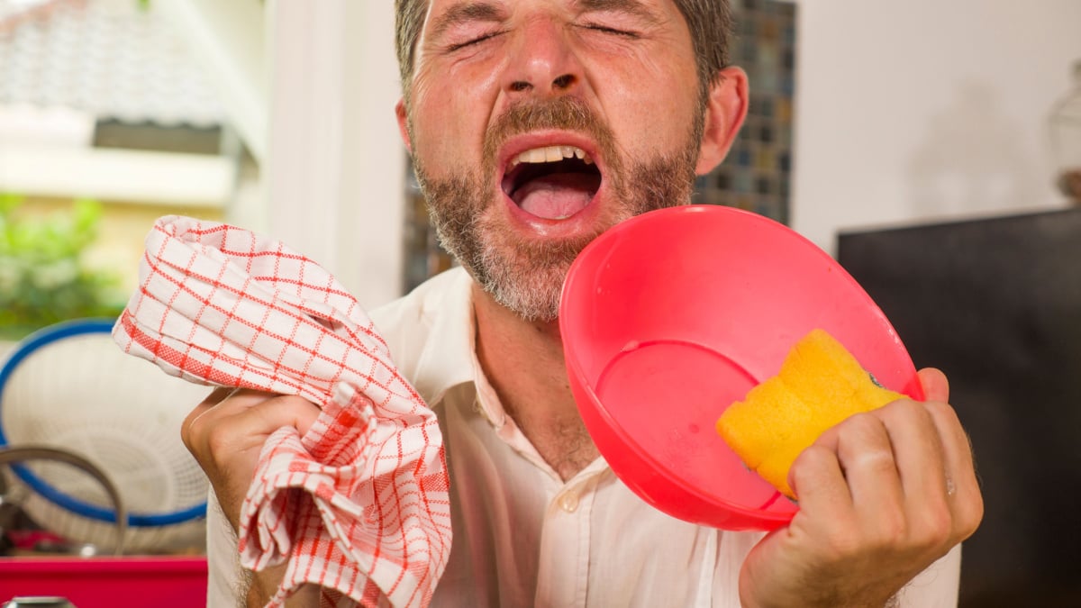 funny lifestyle portrait of mid adult unhappy and stressed man in kitchen apron feeling frustrated and upset overwhelmed by domestic chores washing dishes tired screaming desperate in stress.