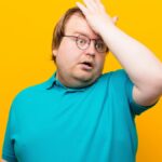 young big size man raising palm to forehead thinking oops, after making a stupid mistake or remembering, feeling dumb against orange wall.