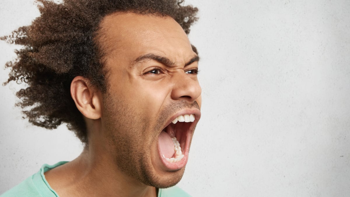 Half profile of aggressive male with dark curly hair, opens mouth widely, screams in panic,