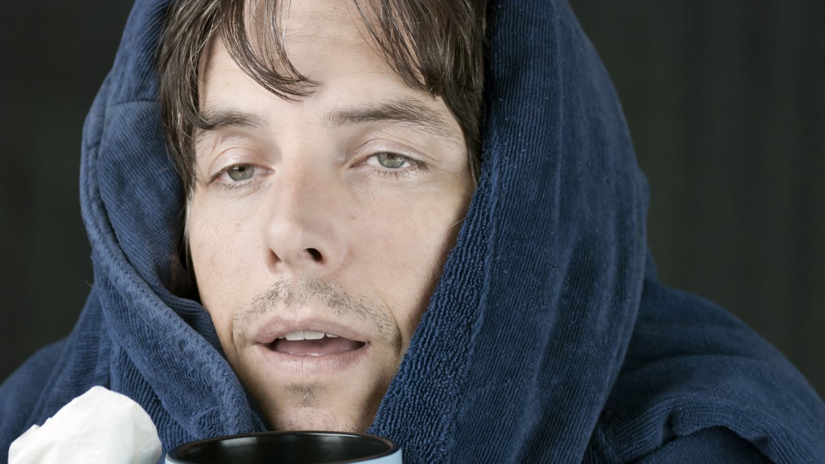 Close-up of a sick man holding a tissue and a hot mug.