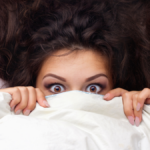 girl in bed with blanket covering half her face