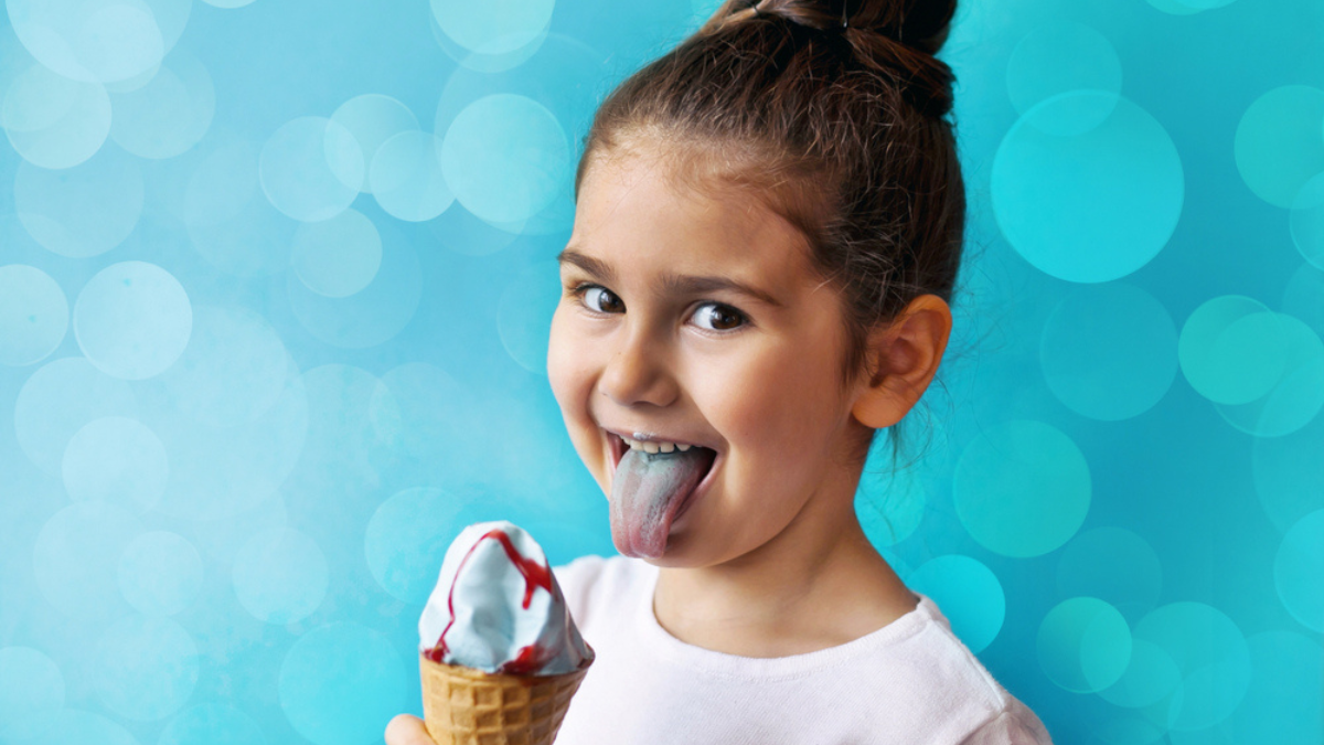 Happy little child girl eating ice cream. Blue background. Light effect.