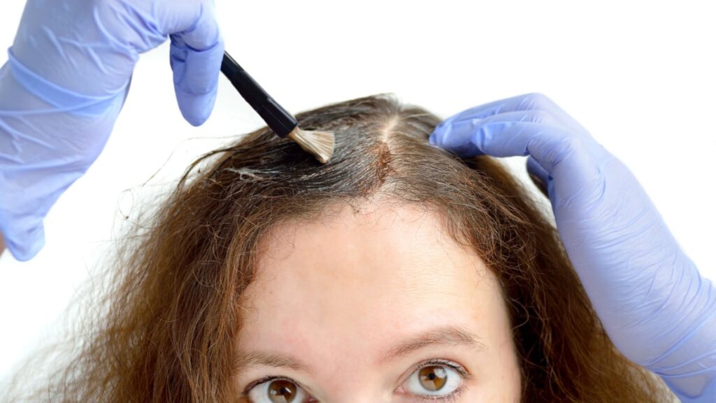 Brunette woman dying her hair with white background.,