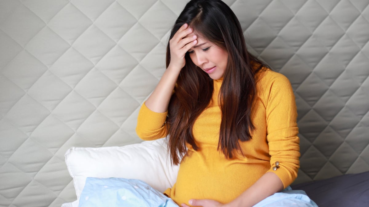 Young asian pregnant woman feeling sick or sad sitting on bed at home.