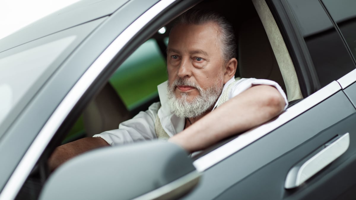 Old stylish good looking man sitting in electrical car near the sport plane.