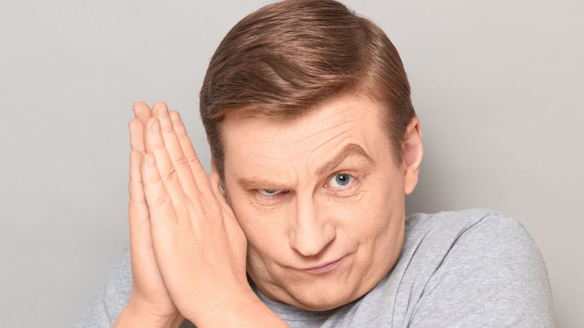 Studio close-up portrait of mature man conspiring and scheming, thinking about sly plan of deception or revenge, looking from under forehead with one eyebrow raised.