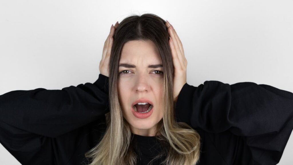 Frustrated girl covering her ears with her hands while screwing her eyes shut as she tries to block sound.