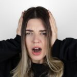 Frustrated girl covering her ears with her hands while screwing her eyes shut as she tries to block sound.