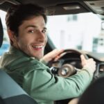 Handsome young man looking back at camera, sitting in car, parking auto, view from rear seat.