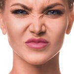 Young beautiful woman over white isolated background smelling something stinky and disgusting, intolerable smell.