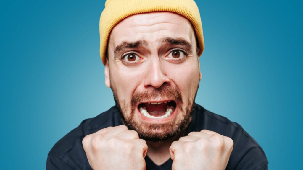A studio shot of a shouting guy, his expression one of anger and irritation as he looks directly at the camera and lets out a violent scream.