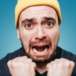 A studio shot of a shouting guy, his expression one of anger and irritation as he looks directly at the camera and lets out a violent scream.