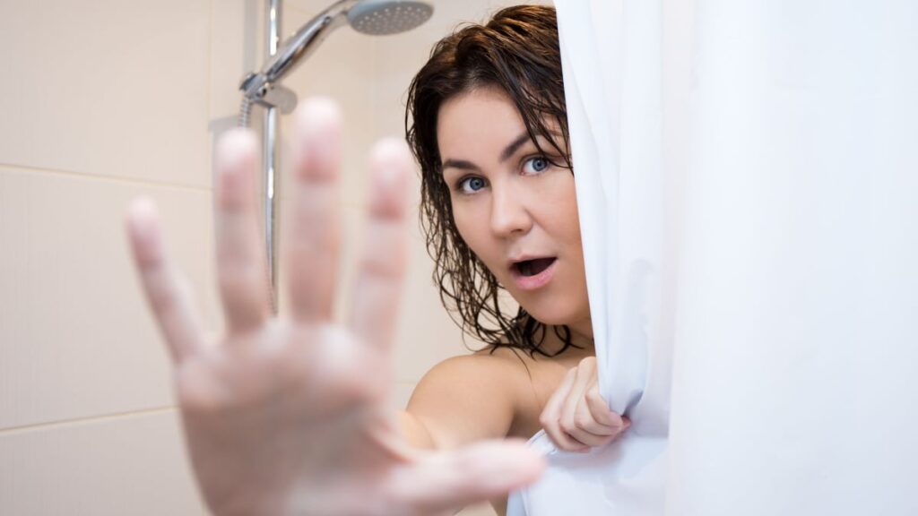 young beautiful woman hiding behind shower curtain.