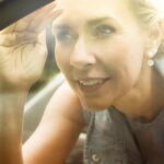 blond woman is looking inside a car through the window.