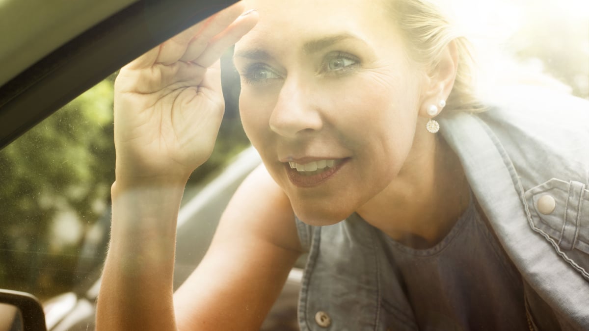 blond woman is looking inside a car through the window.