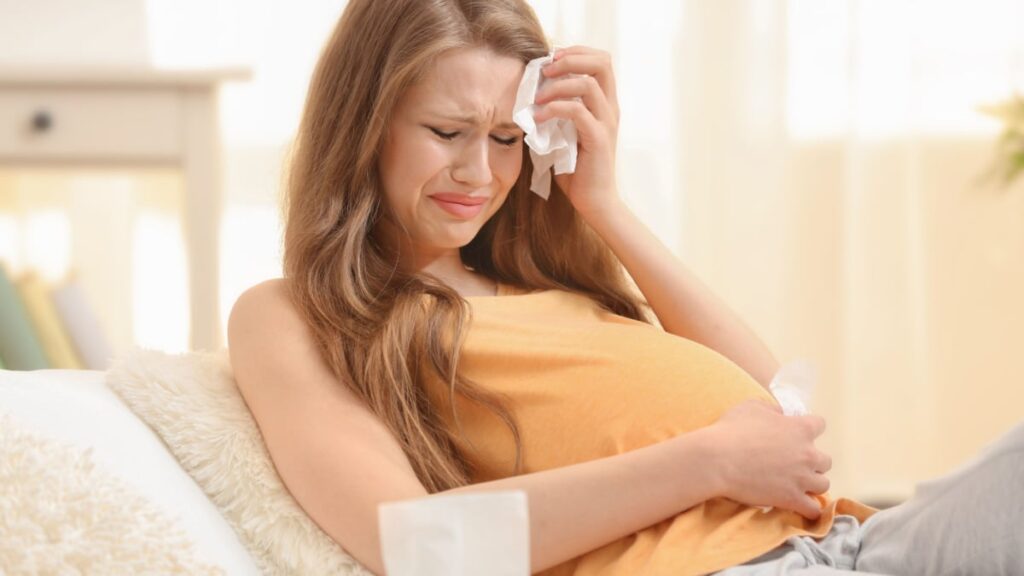 Beautiful pregnant woman crying in light room. Pregnancy hormones concept.