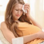 Beautiful pregnant woman crying in light room. Pregnancy hormones concept.