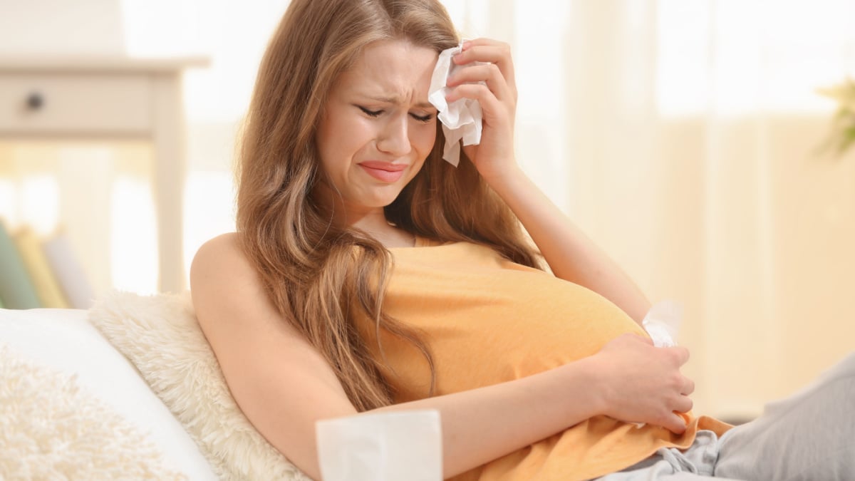 Beautiful pregnant woman crying in light room. Pregnancy hormones concept.