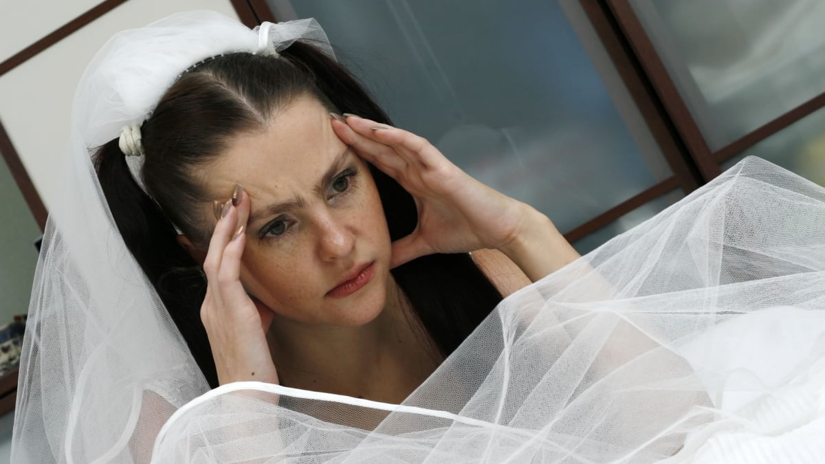 The headache is represented on the face of the beautiful bride in a wedding dress near a bed,