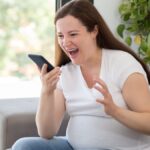 Shot of a furious pregnant woman shouting to smart phone at home.