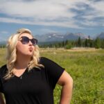 Obnoxious blonde woman does a duck face with pouting lips, hands on hips, in Glacier National Park, near Polebridge, Montana, in a field.
