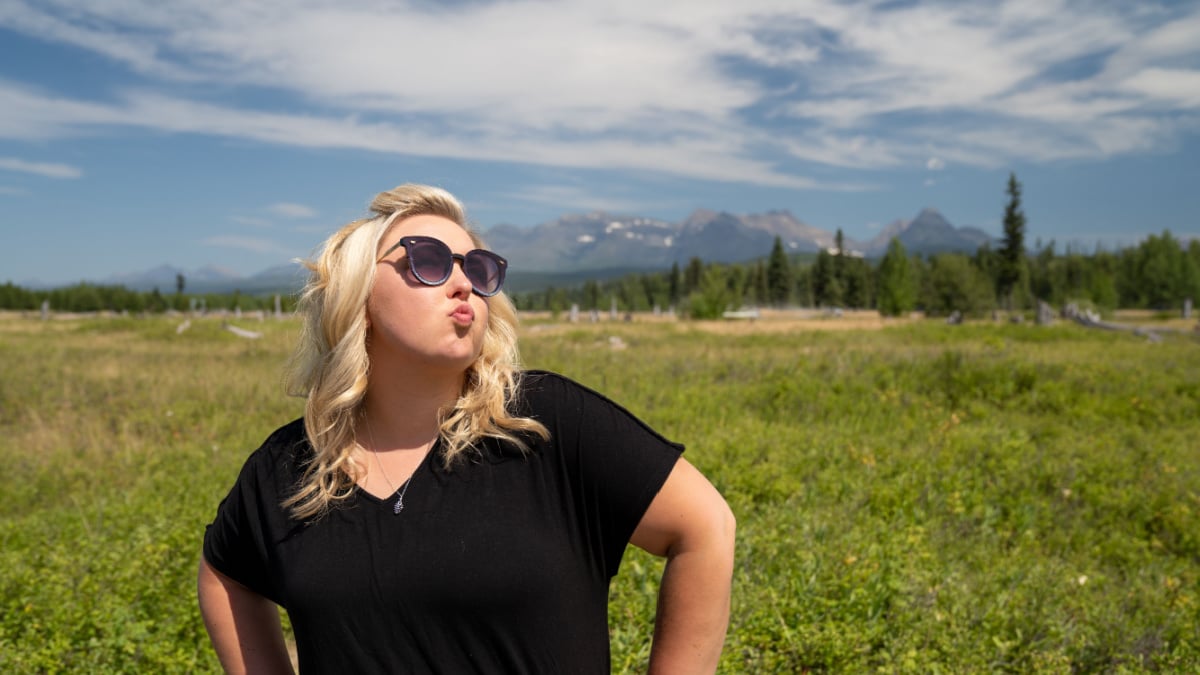 Obnoxious blonde woman does a duck face with pouting lips, hands on hips, in Glacier National Park, near Polebridge, Montana, in a field.