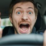 Angry man driving a car. Male driver gesturing and shouting behind the wheel of the car.