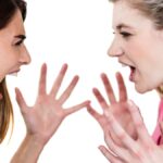 Female friends shouting while standing on white background.