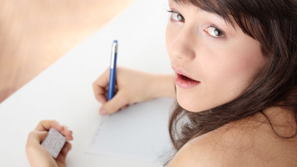 Young caucasian female student stands by school desk and cheat.
