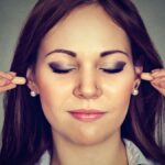 Noise control. Young woman with ear plugs isolated on gray wall background,