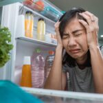 unhappy young asian woman looking inside the fridge.