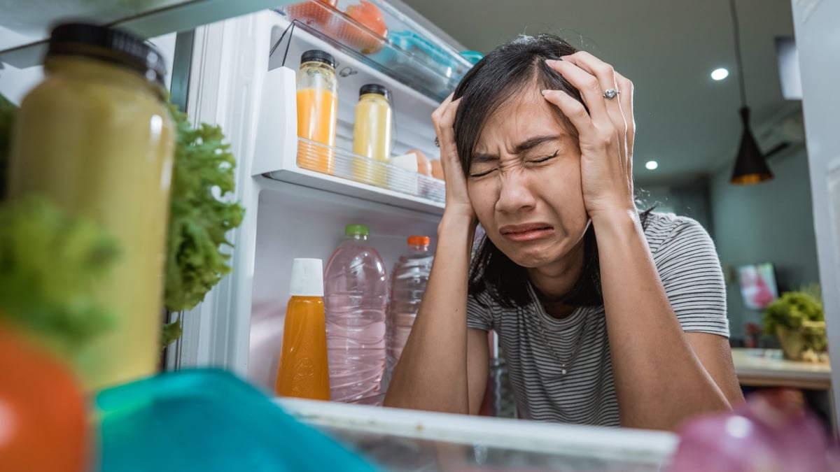 unhappy young asian woman looking inside the fridge.