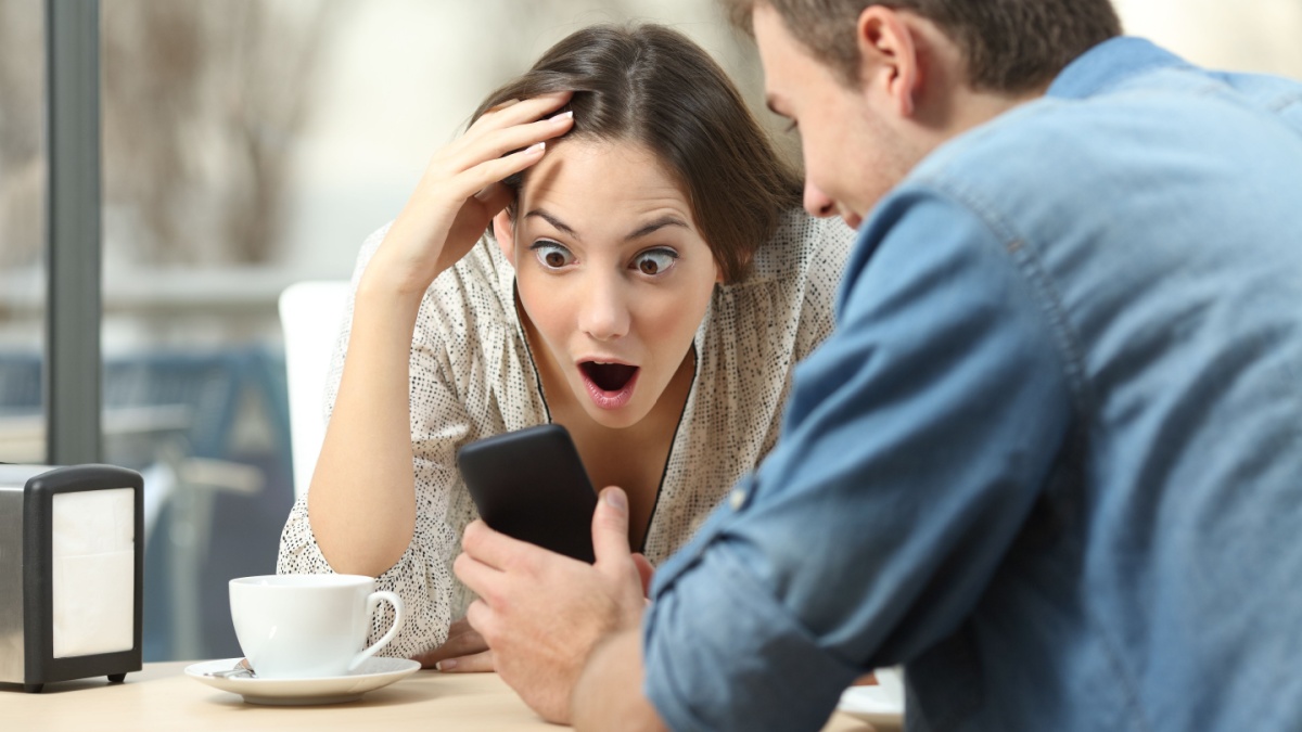 Surprised couple meeting in a coffee shop watching media content in a smart phone.